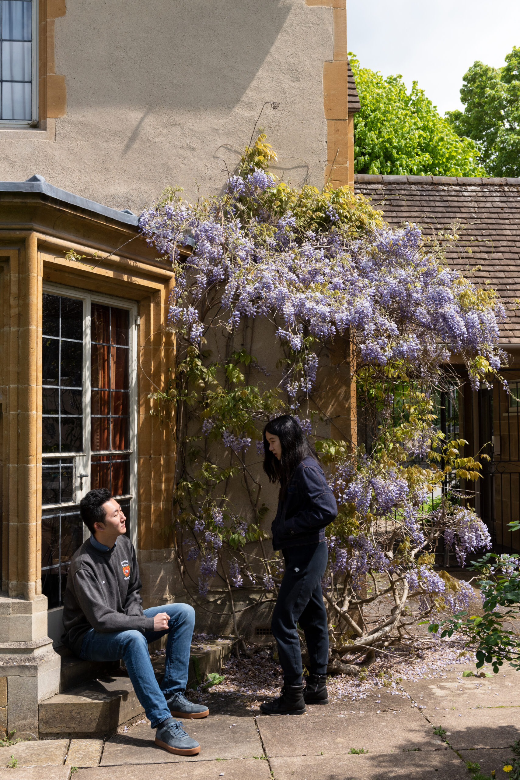 Two students talking next to Wysteria flowers.