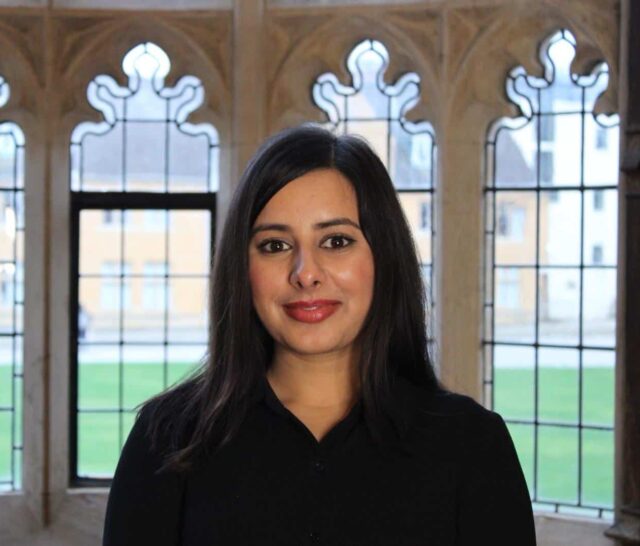 headshot of Asima against the arched windows overlooking Mansfield College quad