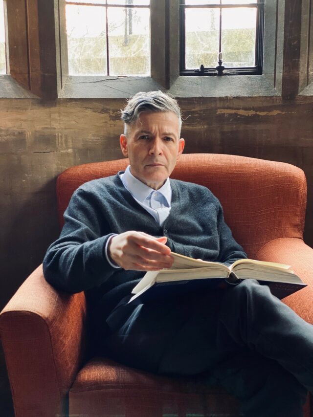 Photo of David sat on an arm chair flicking through a book