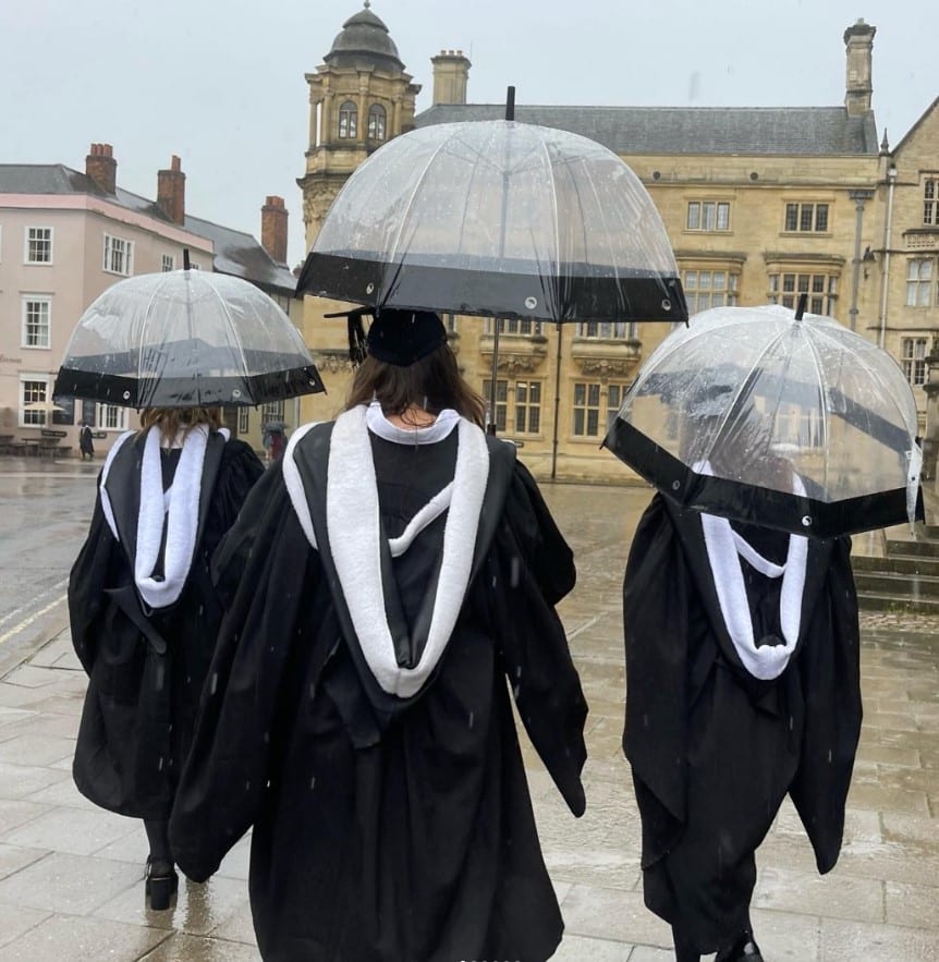 three students with graduation gowns and umbrellas