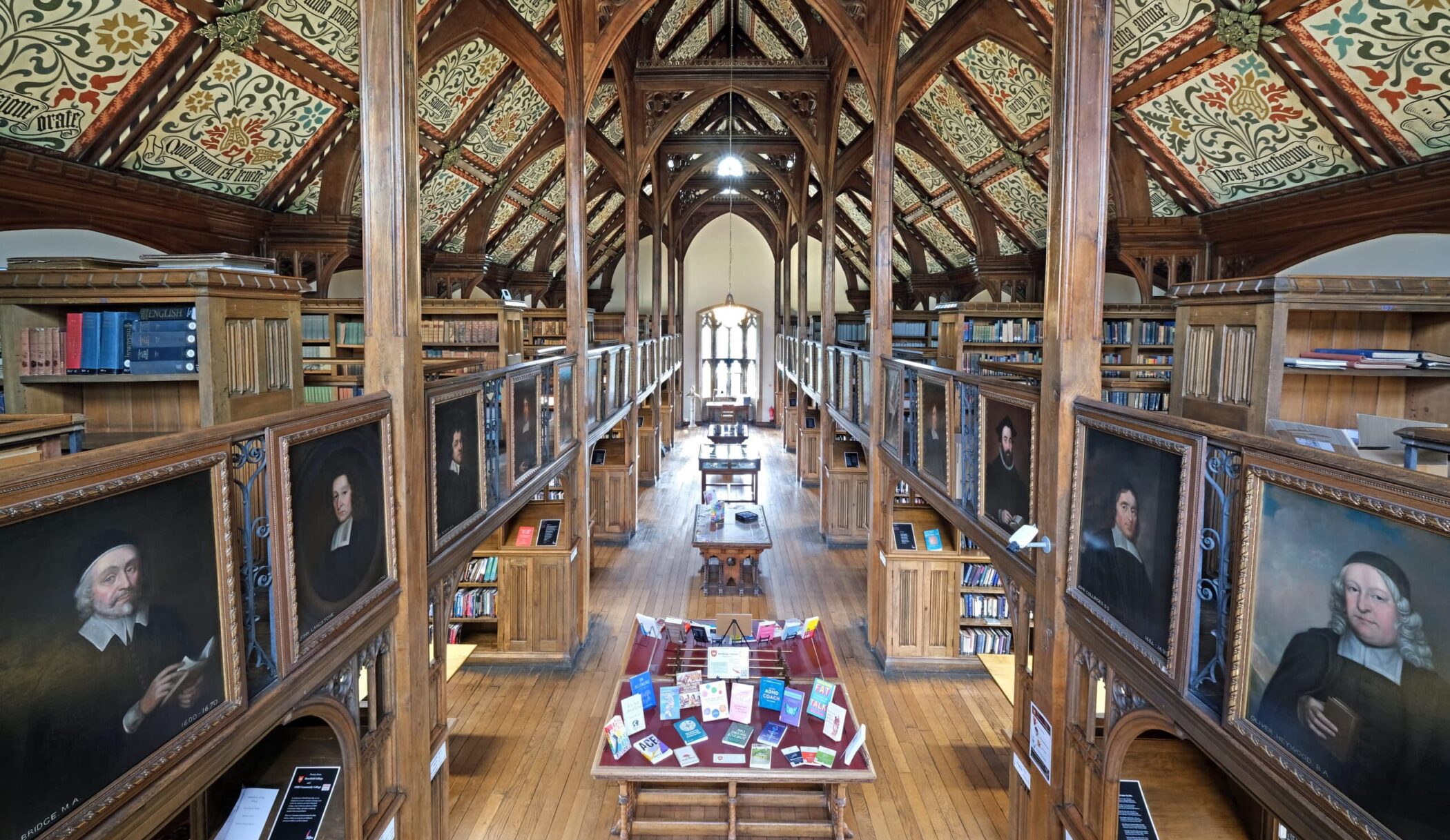 Mansfield College library featuring a painted ceiling, portraits, books, and chairs.
