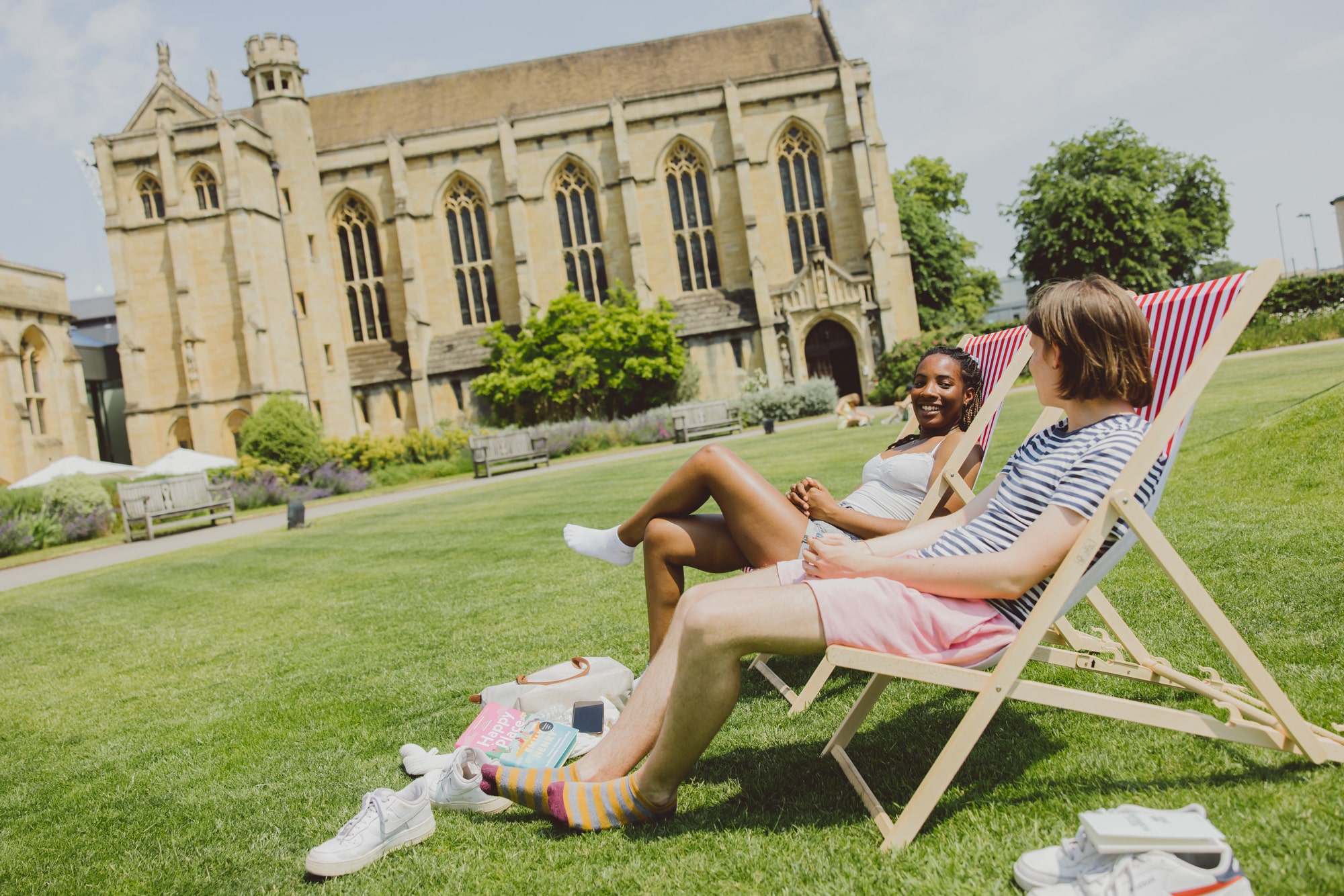 two students on deck chairs in the sunshine on Mansfield quad with the chapel in the back