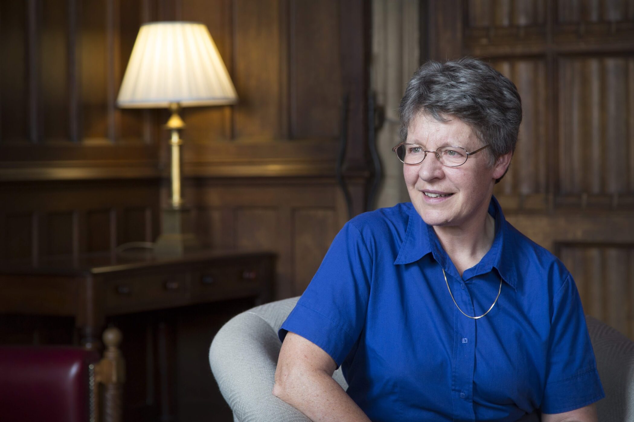 Photo of Jocelyn with her left arm rested on the arm chair while looking to the left. A lampshade appears in the background.