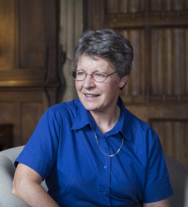 Photo of Jocelyn with her left arm rested on the arm chair while looking to the left. A lampshade appears in the background.